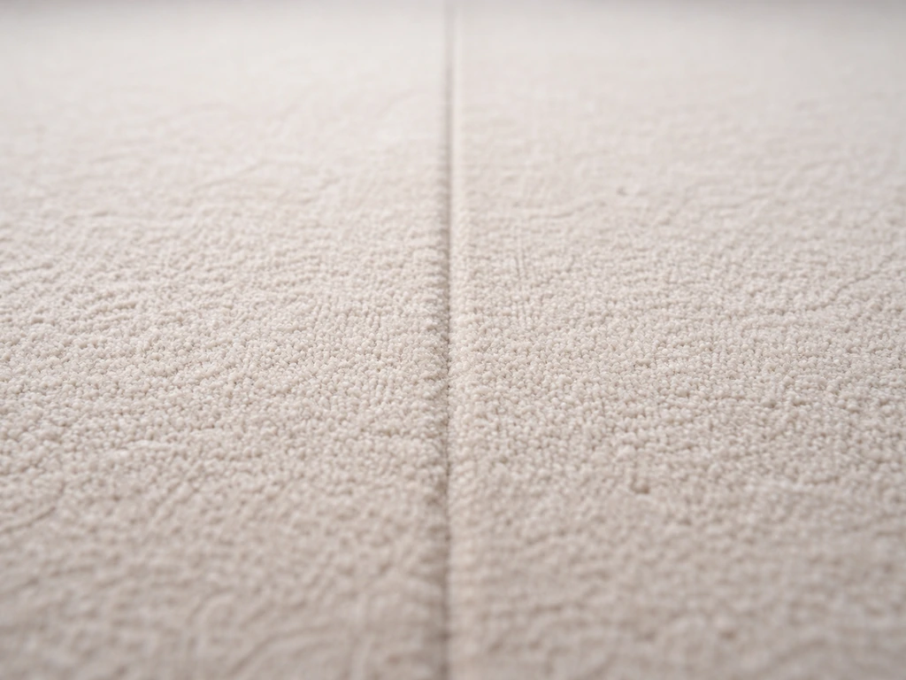 Deux lés de revêtement textile avec fibres alignées, couture discrète entre les bords sur un sol clair.